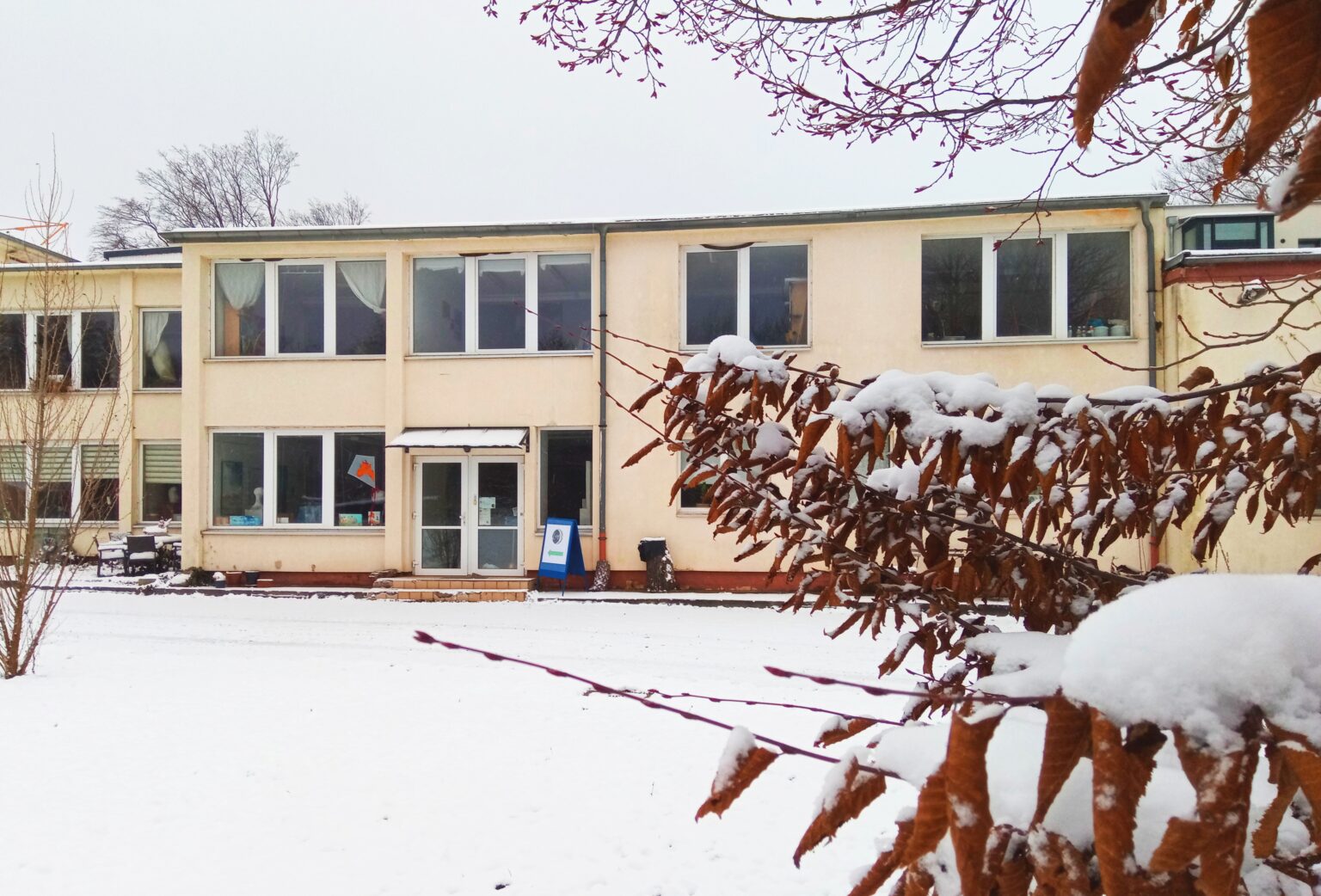 Das Foto bietet eine Frontalansicht des Atelierhauses der Mädlervilla, in dem sich die Vereinsräume von LunA befinden im Dezember 2022. Es liegt Schnee. Im Vordergrund ragen von rechts beschneite Zweige einer Buche mit braunen, zusammengerollten Blättern ins Bild.